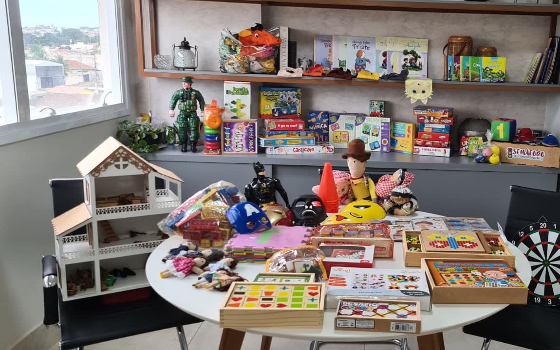 Mesa com jogos, casinha de bonecas, livros infantis e brinquedos terapêuticos para psicoterapia infantil em Jataí